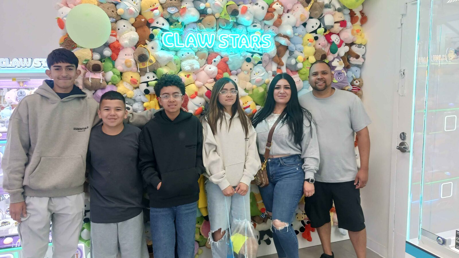 A family of seven smiling under the neon Claw Stars sign at the plushie wall